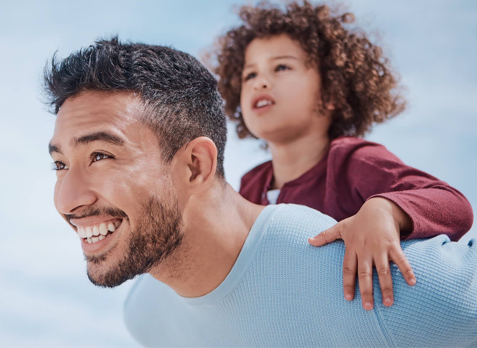 Smiling man giving a piggyback ride to a young child outdoors under a blue sky, capturing the joy and connection that help ease physician burnout.
